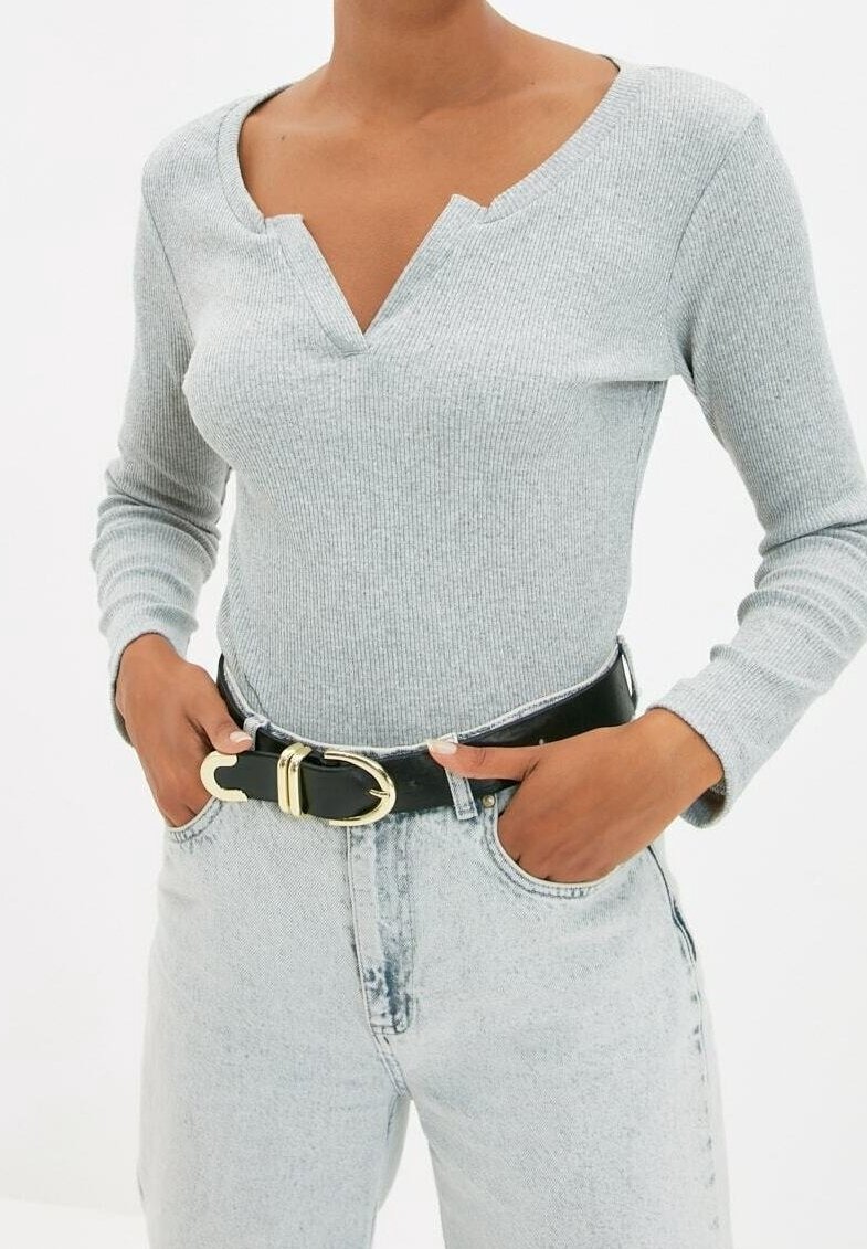 Personne portant un haut à manches longues côtelé gris clair avec un col en V en encoche, un jean taille haute délavé clair et une ceinture noire avec une boucle dorée.
