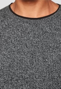 Pull gris avec une finition texturée, doté d'un col côtelé noir et une vue rapprochée du motif et du tissage du tissu.