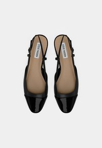 Fekete lakkbőr pántos cipők négyzet alakú orral, minimális pántokkal és sima belsővel, bézs talpbetéttel, amely márkajelzéssel van ellátva.