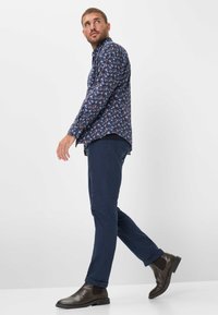Marineblaues Langarmhemd mit floralem Muster, kombiniert mit dunkelblaue Slim-Fit-Hose und braunen Leder-Chelsea-Boots.