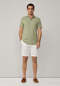Ljusgrön pikétröja med krage, parat med vita shorts. Modellen bär bruna slip-on skor, mot en neutral bakgrund.