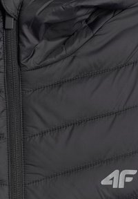 Section de veste matelassée noire avec fermeture éclair et logo réfléchissant "4F" en bas à droite.