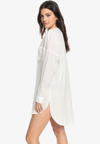 Camicia bianca in lino oversize con maniche lunghe, polsini con bottone e tasca frontale. Presenta spacchi laterali per una vestibilità comoda.