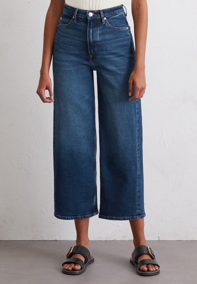 Hoch taillierte, weit geschnittene blaue Jeans aus Denim mit glatter Oberfläche, fünf Taschen und sichtbarem Knopfverschluss am Bund.