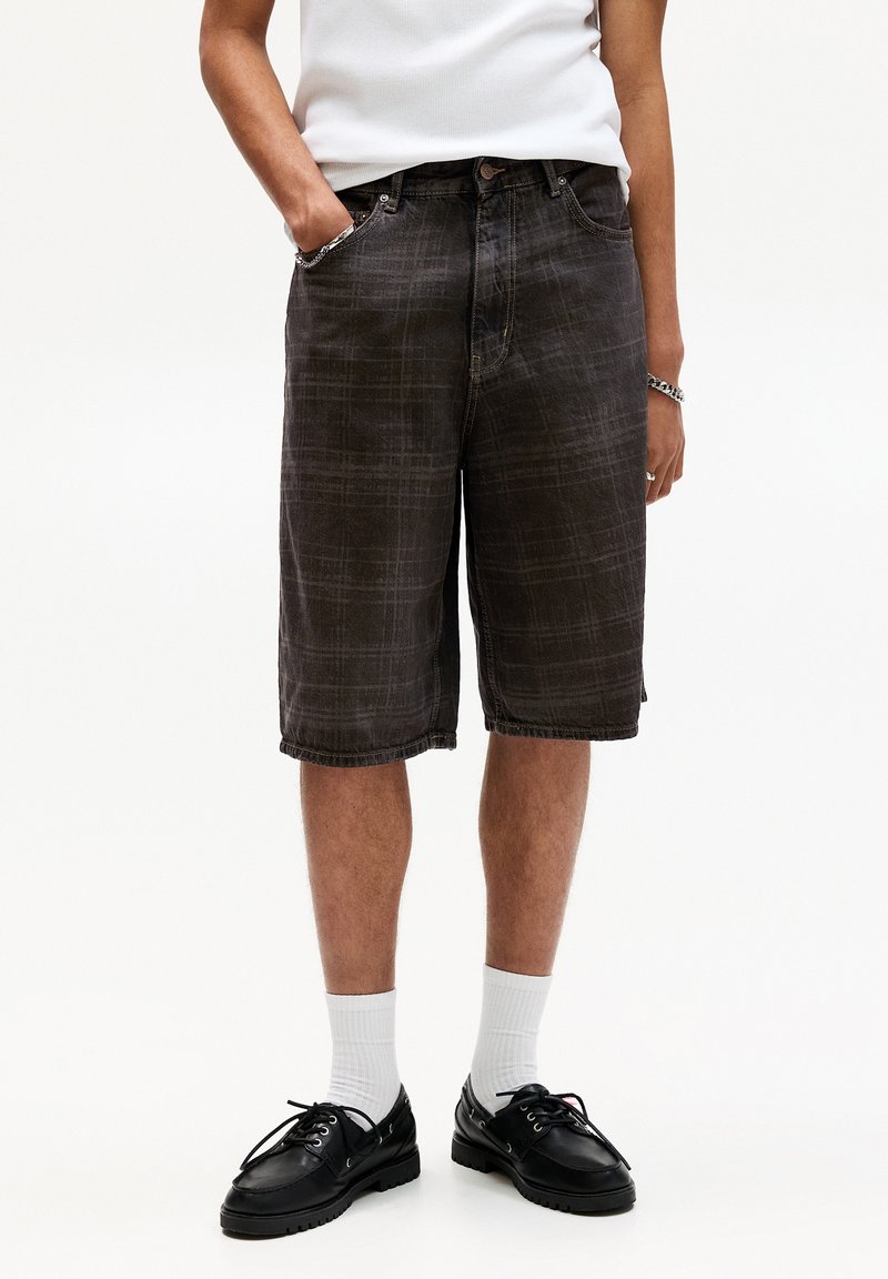 Zwarte geruite denim shorts met een rechte snit, voorkruizen en een licht gerafeld zoom. Gecombineerd met zwarte schoenen en witte sokken.