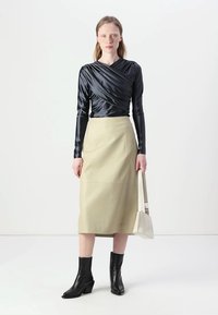 Svart satin langermet topp med drapert detalj, paret med et kne-langt beige skinnskjørt. Brukt med svarte hælsko og en lys veske.