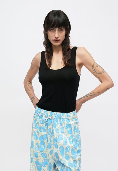 Μαύρο αμάνικο τοπ σε συνδυασμό με ανοιχτόχρωμο μπλε παντελόνι με σχέδιο και ελαστική μέση. Το ύφασμα φαίνεται λείο και ελαφρύ.
