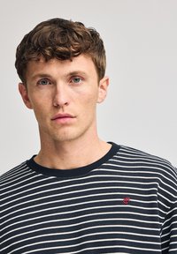 Marinblå och vit randig bomullströja med rundad halsringning och en liten röd logga på bröstet, med ett mjukt och strukturerat tyg.