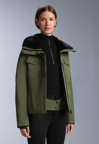 Olive zelena jakna z umetnim krznom na ovratniku, ki ima žepe s pritisnimi gumbi, zadrgo in prilegajočo črno osnovno plast pod njo.