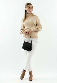 Suéter beige de canalé, pantalones blancos con dobladillo deshilachado, botines marrones hasta el tobillo y un pequeño bolso negro de hombro con solapa. Diseño simple y limpio.