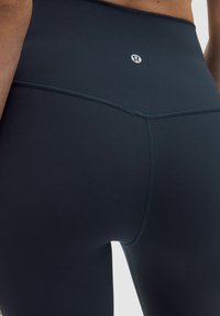 Sötét navy színű, magas derekú leggings, sima textúrával, sík varrásokkal és egy kis logó díszítéssel a hátsó derekán.