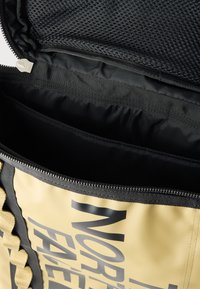 Μπεζ και μαύρο σακίδιο με μερικώς ανοιχτό φερμουάρ που αποκαλύπτει μαύρο μαλακό εσωτερικό με επένδυση και δίχτυνη τσέπη μέσα στο καπάκι.