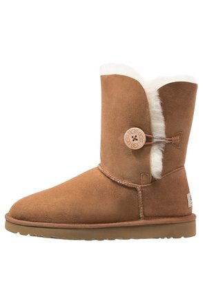 Mid-calf tan suede boot with shearling lining, button closure on side, flat rubber sole, and UGG logo on heel tab.