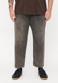 Pantaloni din denim negru, îmbătrâniți, cu o croială relaxată, prezentând un picior drept și margini desfăcute, asortați cu adidași negri.