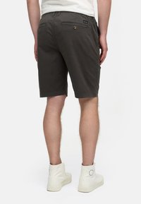 Shorts gris foncé en coton mélangé, présentant une coupe mi-longue, deux poches arrière avec boutons et des poches latérales. Baskets montantes blanches.