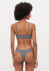 Szürke, két részes fehérnemű szett, amely tartalmaz egy bralette-t vékony, állítható pántokkal és egy illő tanga bugyit. Puha, textúrált anyag, minimális varratokkal.