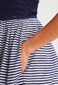 Handen i fickan på en marinblå och vit horisontellt randig kjol med en solid marinblå topp.