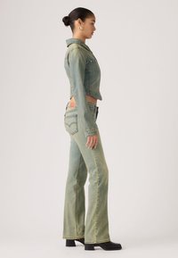 Ανοιχτό πράσινο τζιν μπουφάν με κομμένο σχεδιασμό και κανονικό γιακά, συνδυασμένο με ανοικτό πράσινο τζιν παντελόνι με καμπάνα. Και τα δύο έχουν λεπτομέρειες ραφής.