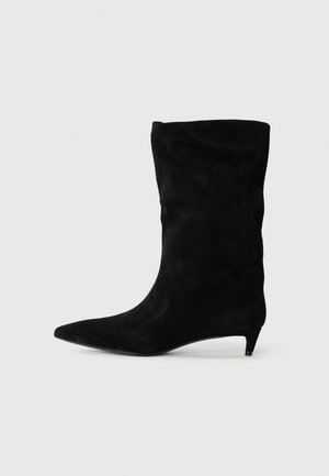 Stivale alla caviglia in suede nero con punta affusolata e tacco kitten basso, caratterizzato da un design morbido e una texture liscia.