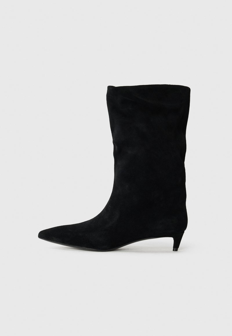 Stivale alla caviglia in suede nero con punta affusolata e tacco kitten basso, caratterizzato da un design morbido e una texture liscia.