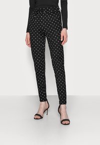 Svarta byxor med prickar som har en åtsittande design, elastisk midja och dragsko. Matchas med svarta högklackade sandaler.