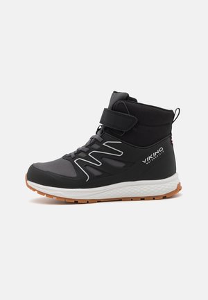 Bota impermeable vikinga de caña alta en negro y gris con suela blanca, banda de velcro naranja, suela con dibujo y diseño con cordones vista de lado.