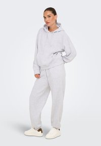 Felpa grigio chiaro e pantaloni della tuta coordinati realizzati in un tessuto morbido, con tasca a marsupio e cordini, abbinati a sneaker bianche.
