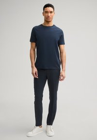 Granatowa koszulka typu crew neck z bawełny, zestawiona z dopasowanymi ciemnymi spodniami i białymi trampkami. Prosty design, bez widocznych wzorów czy logo.