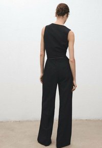 Black pinstriped jumpsuit with a fitted bodice, sleeveless design, wide legs, and a belted waist. Texture appears smooth and tailored.