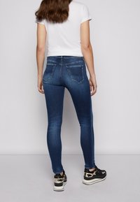 Vaqueros ajustados de denim azul oscuro con una textura suave, que cuentan con una cintura de altura media y bolsillos traseros, combinados con zapatillas negras y doradas.