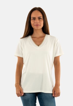 Camiseta blanca de manga corta con escote en V y cuello texturizado, combinada con jeans azules. Tejido suave, ajuste relajado, con un minimalismo en los detalles.