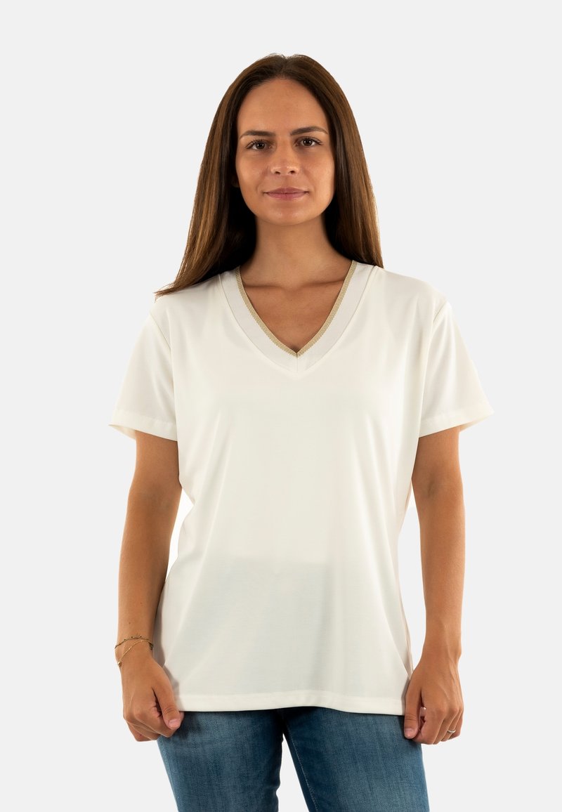 Camiseta blanca de manga corta con escote en V y cuello texturizado, combinada con jeans azules. Tejido suave, ajuste relajado, con un minimalismo en los detalles.