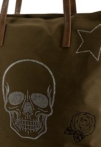 Bolso tote de color verde oliva con un diseño de calavera que incluye cristales de imitación, acompañado de un gráfico de rosa negra y un acento de estrella. Asas de cuero marrón.
