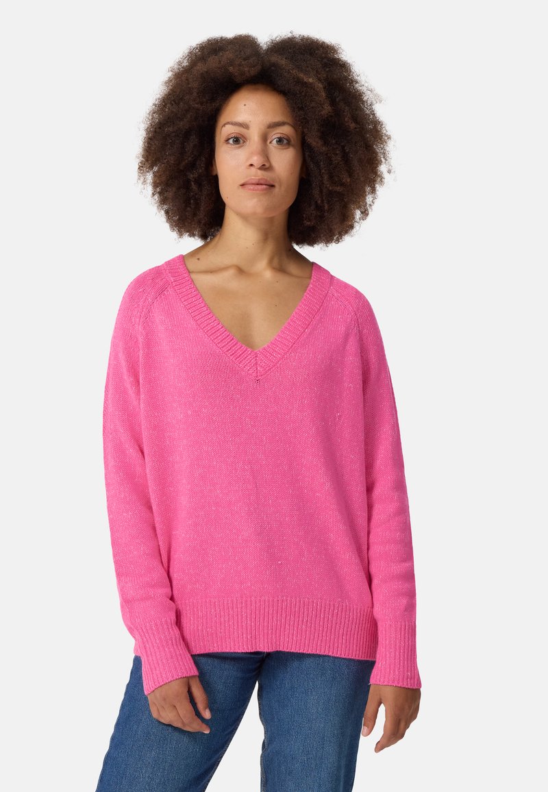 Roze V-hals trui met lange mouwen en geribde manchetten. Textuurstof met een lichte glans. Gepaard met blauwe spijkerbroek.