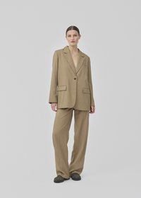 Blazer oversize beige avec des revers et deux poches avant, associé à un pantalon large assorti et des chaussures noires à enfiler. Texture lisse.