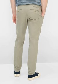 Beige slimfitbroek met een gladde textuur, voorzien van achterzakken met knoopsluitingen, gecombineerd met donkerblauwe sneakers.