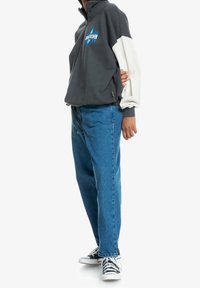 Pullover in pile grigio e bianco con mezza zip e logo grafico, abbinato a jeans in denim blu a gamba dritta e sneaker in bianco e nero.