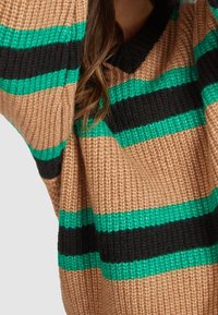 Pull en tricot avec des rayures horizontales en beige, noir et teal. Design en V avec une coupe loose et un tissu texturé.