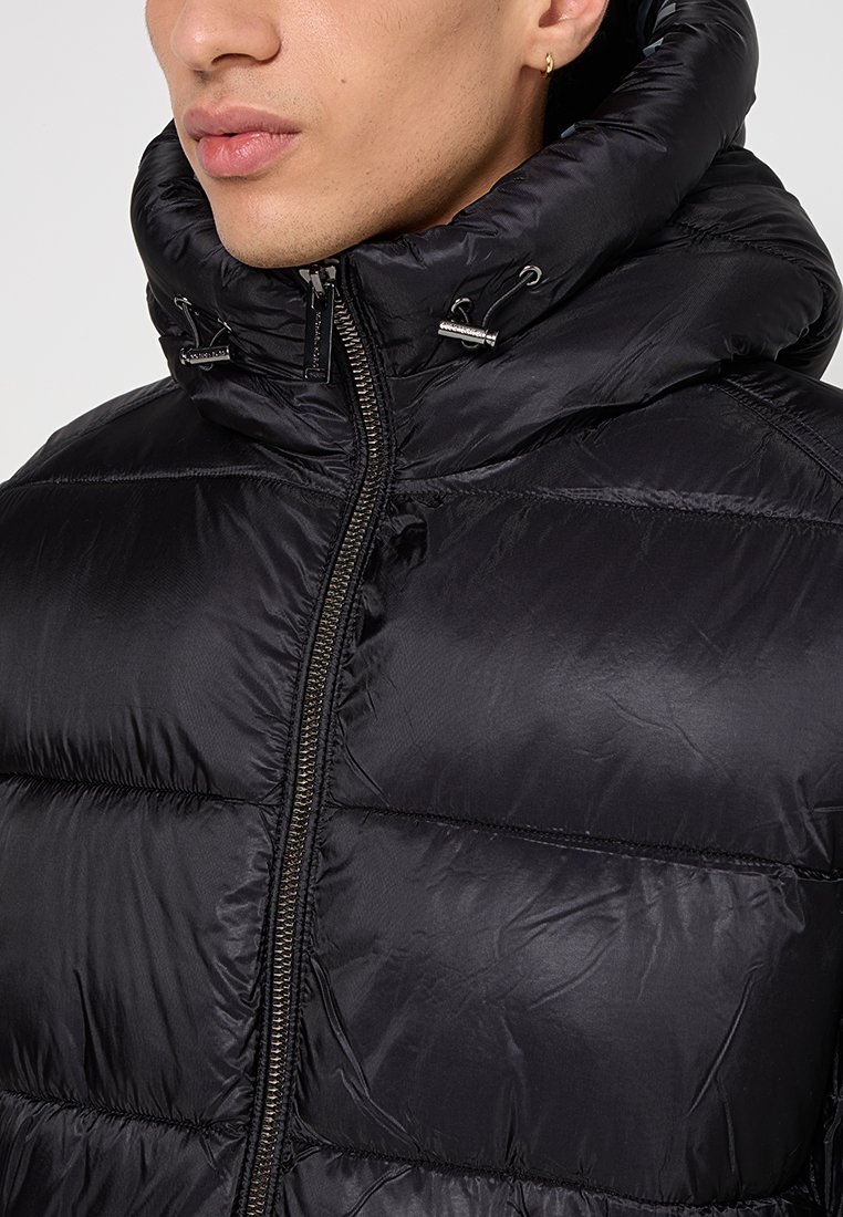 Giubbotto piumino nero con colletto alto e chiusura con zip. Realizzato in tessuto lucido e trapuntato con una texture liscia e dettagli con cordoncino.
