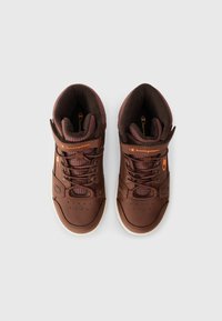 Zapatillas altas marrones hechas de materiales de cuero y malla, con un collar acolchado, diseño de cordones, correa ajustable y suela de goma blanca.
