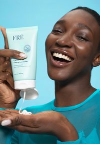 Miętowo-zielona tubka żelu do twarzy z białą nakrętką; trzymana w dłoni, wydobywa się krem; modelka ubrana w przezroczysty turkusowy top.