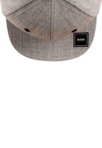 Grå caps laget av teksturert stoff med flat skjerm. Har et svart firkantet merke med "MSTRDS"-logo. Inkluderer ventilasjonshull på sidene.