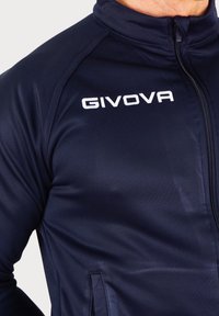 Temno modra Givova jakna z zadrgo in visokim ovratnikom, narejena iz gladkega materiala. Ima stranske žepe in vezeno logo na prsih.