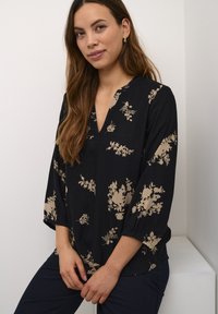 Must mustriga mustaga mustri ja kolmeveerandi varrukatega must blouse. Materjal näeb välja kerge ja tekstuuriga.