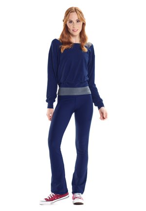 Maglia a maniche lunghe blu navy con un bordo grigio aderente, abbinata a pantaloni blu navy; modello che indossa scarpe da ginnastica rosse e bianche.