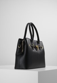 Svart läderhandväska med en strukturerad form, guldhardwaredetaljer, dubbla handtag och ett zippered fack. Texturerad yta på materialet.