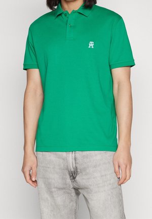 Zelená bavlněná polo tričko s klasickým límečkem, krátkými rukávy a malým bílým logem na levé hrudi, doplněné o šedé denimové džíny.