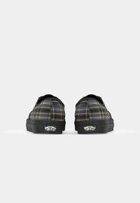 Black and yellow plaid slip-on shoes with a rubber sole, rounded toe, and Vans logo on the heel. Textured fabric with stitching detail.