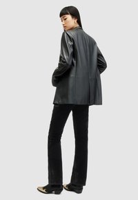 Blazer in pelle nera con vestibilità rilassata, dotato di maniche lunghe e revers a punta, abbinato a pantaloni in velluto nero a palazzo e scarpe con tacco.