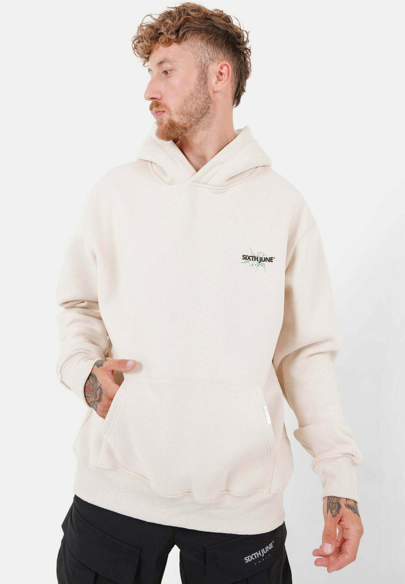 Felpa beige con cappuccio, tasca frontale, dettagli a coste ai polsini e un piccolo logo sul petto. Texture morbida, design casual.